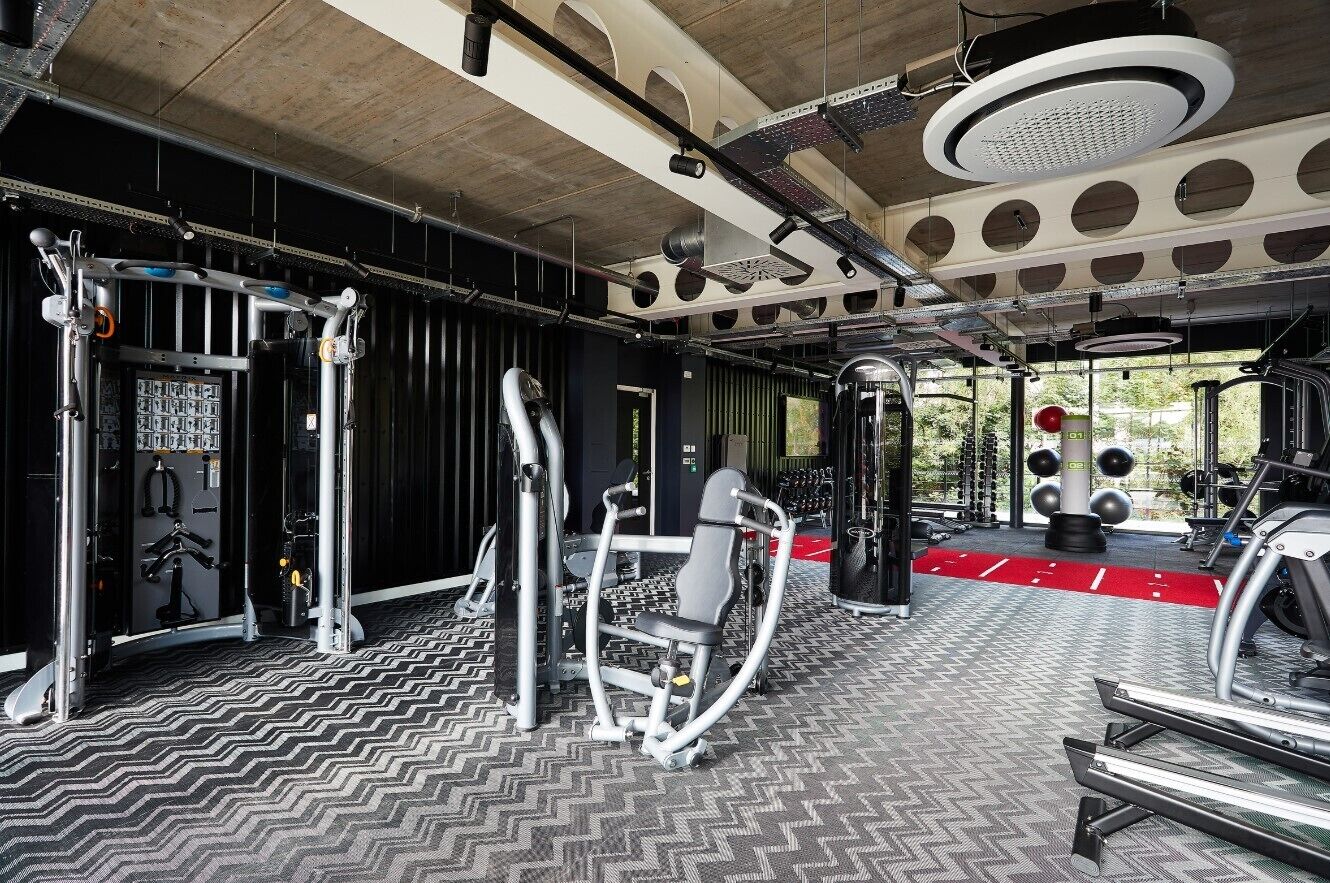 Un gimnasio con diferentes equipos de ejercicio, piso estampado y techo con lámparas circulares.