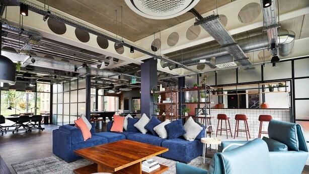 A modern interior with a blue sofa set, a wooden coffee table, and a bar area with stools. - Student Only Vita Pebble Mill (Birmingham)