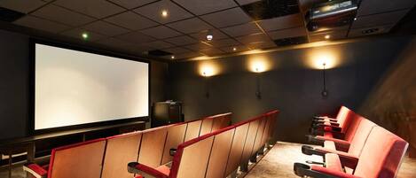 A movie theater with rows of red seats, a large screen, and ceiling lights.