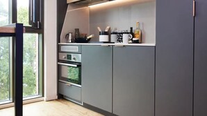 A modern kitchen with grey cabinets, a built-in oven, and a window providing a view of greenery outside. - Student Only Vita Pebble Mill (Birmingham)