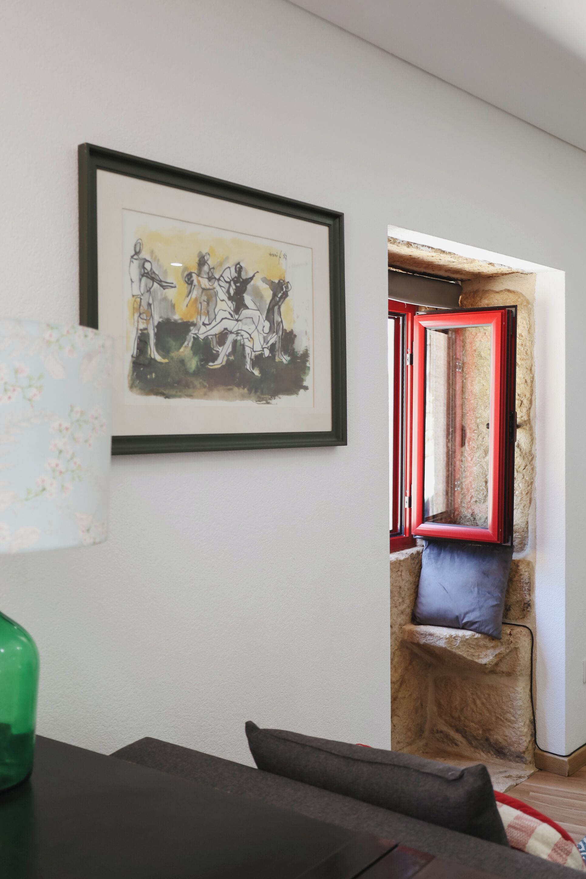 Ein Zimmer mit einem gerahmten abstrakten Gemälde, einem fensterartigen Element mit rotem Rahmen, einer Steinwand und einem dunkelgrauen Sofa.