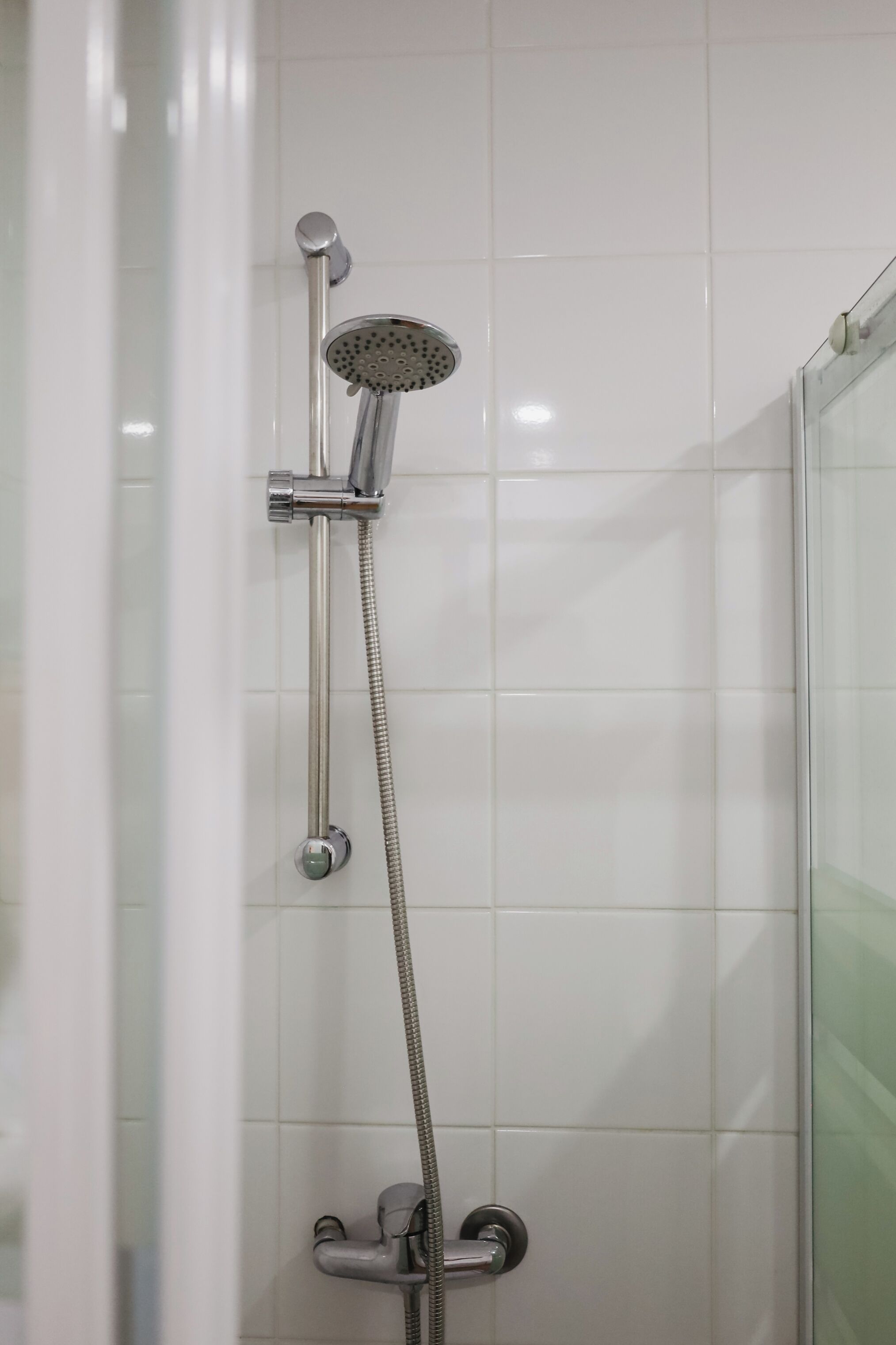 A shower with a handheld showerhead and a fixed showerhead, both mounted on a wall with white tiles.