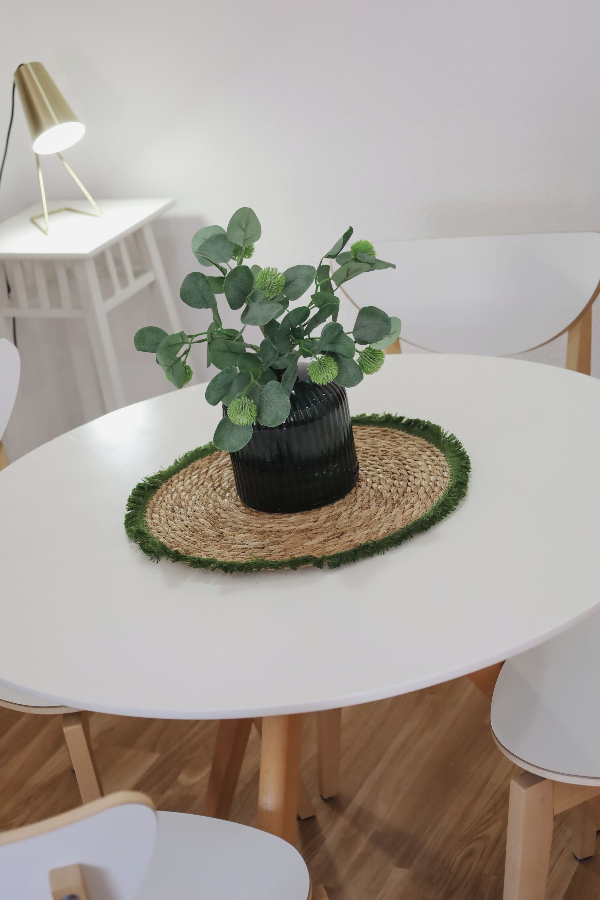 A round white table with a woven placemat and a potted plant.