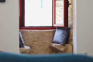 Un banco de piedra con cojines, una ventana con marco rojo y una vista parcial de una pared.