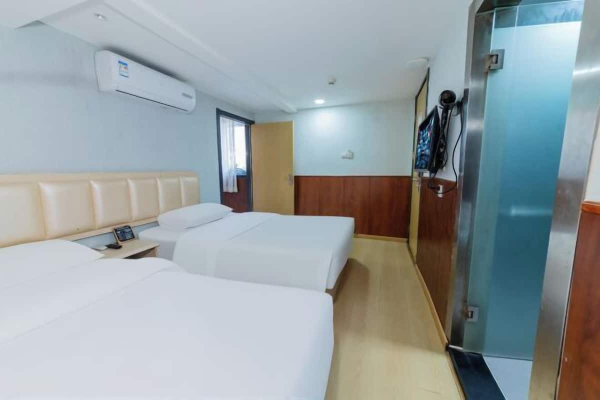 Quarto de hotel com duas camas, cabeceira de madeira, mesa de cabeceira pequena, ar condicionado e uma porta com espelho e telefone.