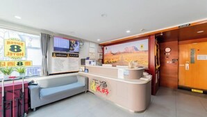 Un espace d’accueil d’hôtel comprenant un canapé, un comptoir de réception, un écran de télévision et une fresque murale sur le thème du désert.