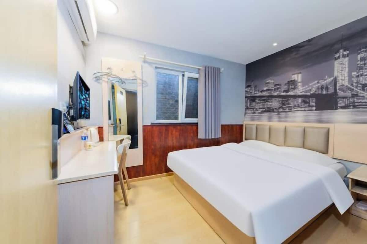 Quarto de hotel com cama, escrivaninha, cadeira, janela com cortinas e um mural com vista para a cidade.