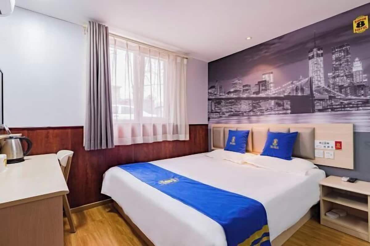 Quarto de hotel com cama, escrivaninha, cadeira, janela com cortinas e um mural com vista para a cidade.