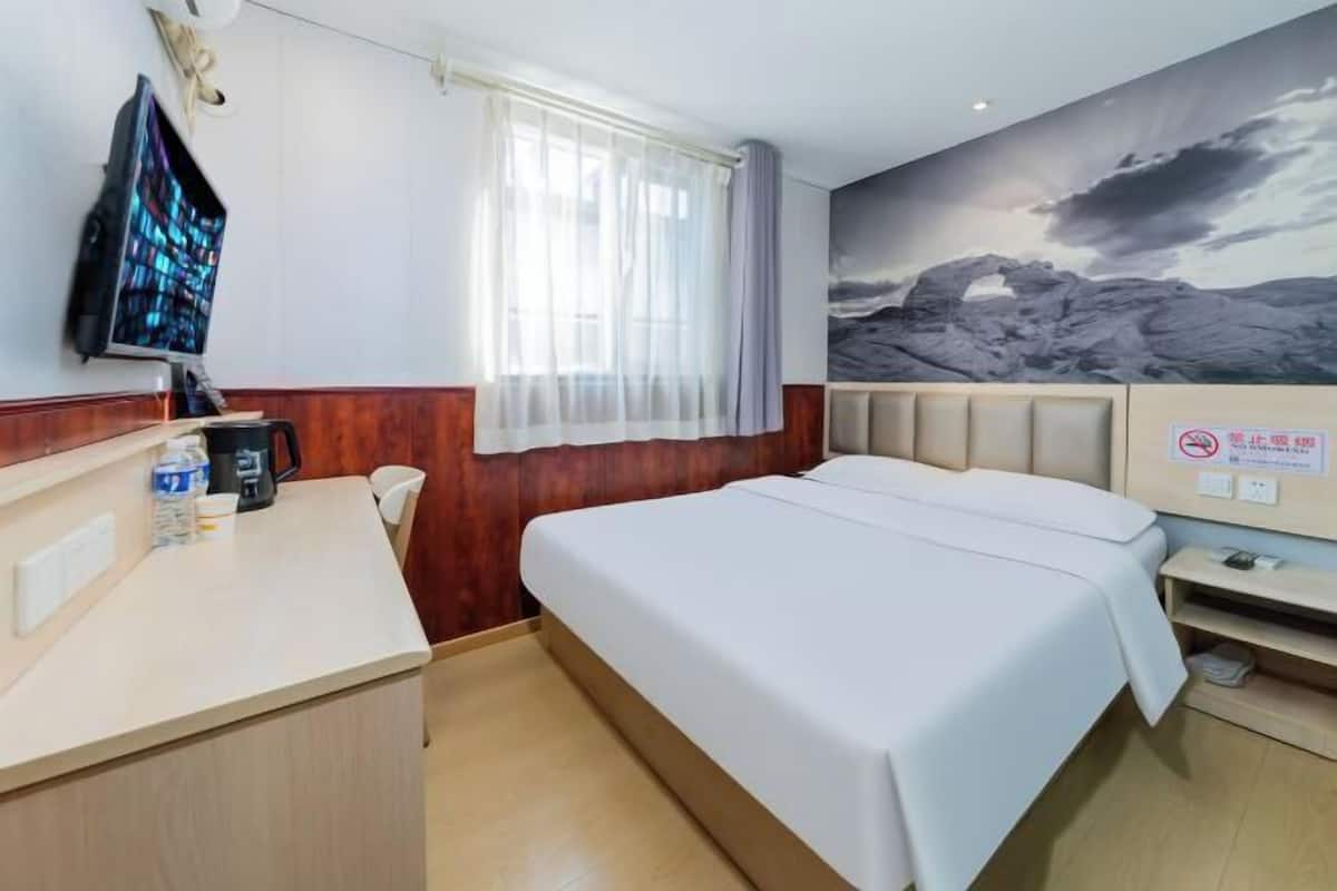 Quarto de hotel com uma cama, uma escrivaninha com computador, janela com cortinas e televisão fixada na parede.
