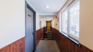 Un couloir d’hôtel avec un plancher en bois, une porte portant l’inscription « 202 » et une fenêtre sur le côté droit.