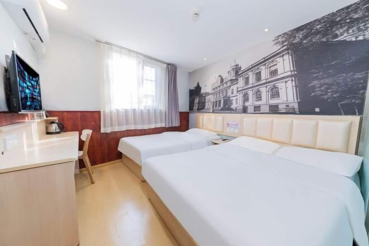 Quarto de hotel com duas camas, uma escrivaninha, uma televisão e um mural na parede.
