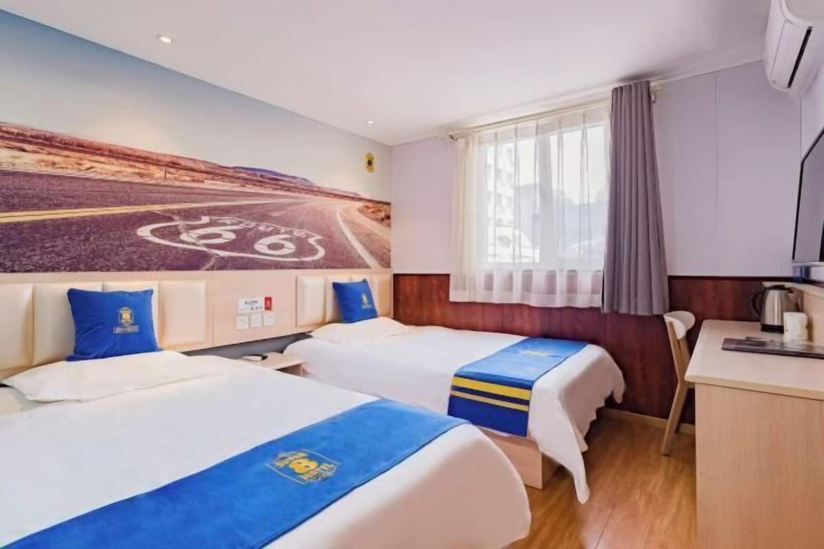 Quarto de hotel com duas camas, uma escrivaninha, uma janela com cortinas e um mural na parede.