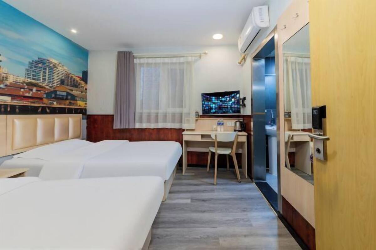 Quarto de hotel com duas camas, uma escrivaninha, uma cadeira, uma televisão e um mural com vista para a cidade.