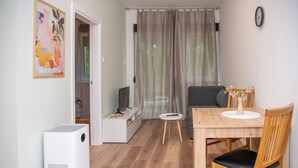 Ein gemütlicher Wohnbereich mit Essplatz, einer Couch, einem Fernseher und einem Fenster mit Vorhängen.