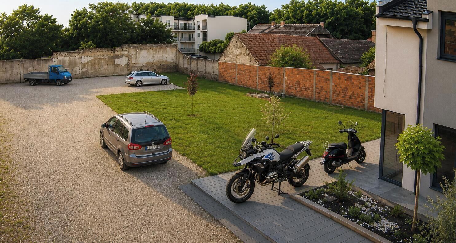 Zona residencial con camino pavimentado, un auto estacionado, una motocicleta y una camioneta azul.