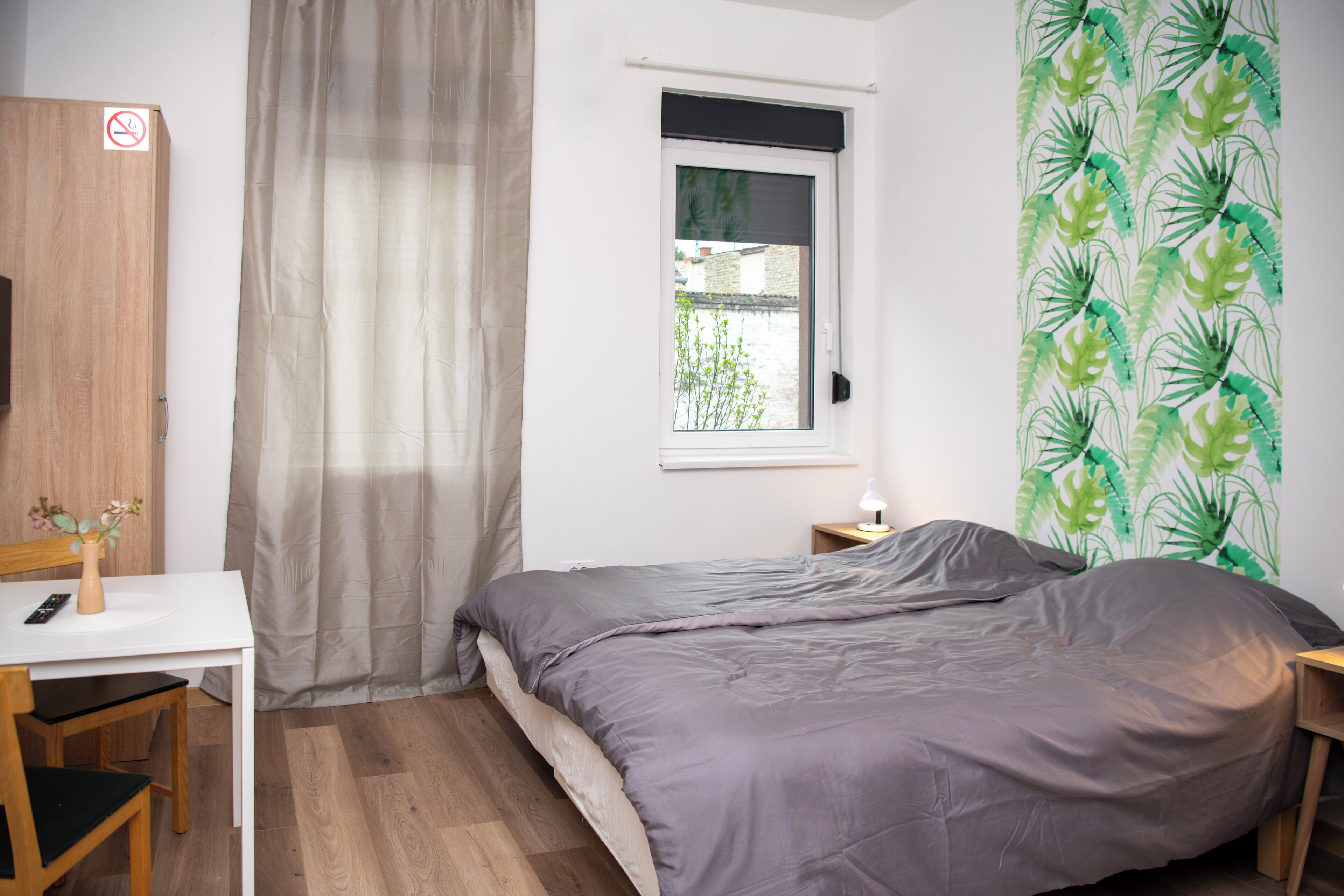 Un dormitorio con cama, escritorio, silla, ventana con vistas y pared con diseño de hojas.