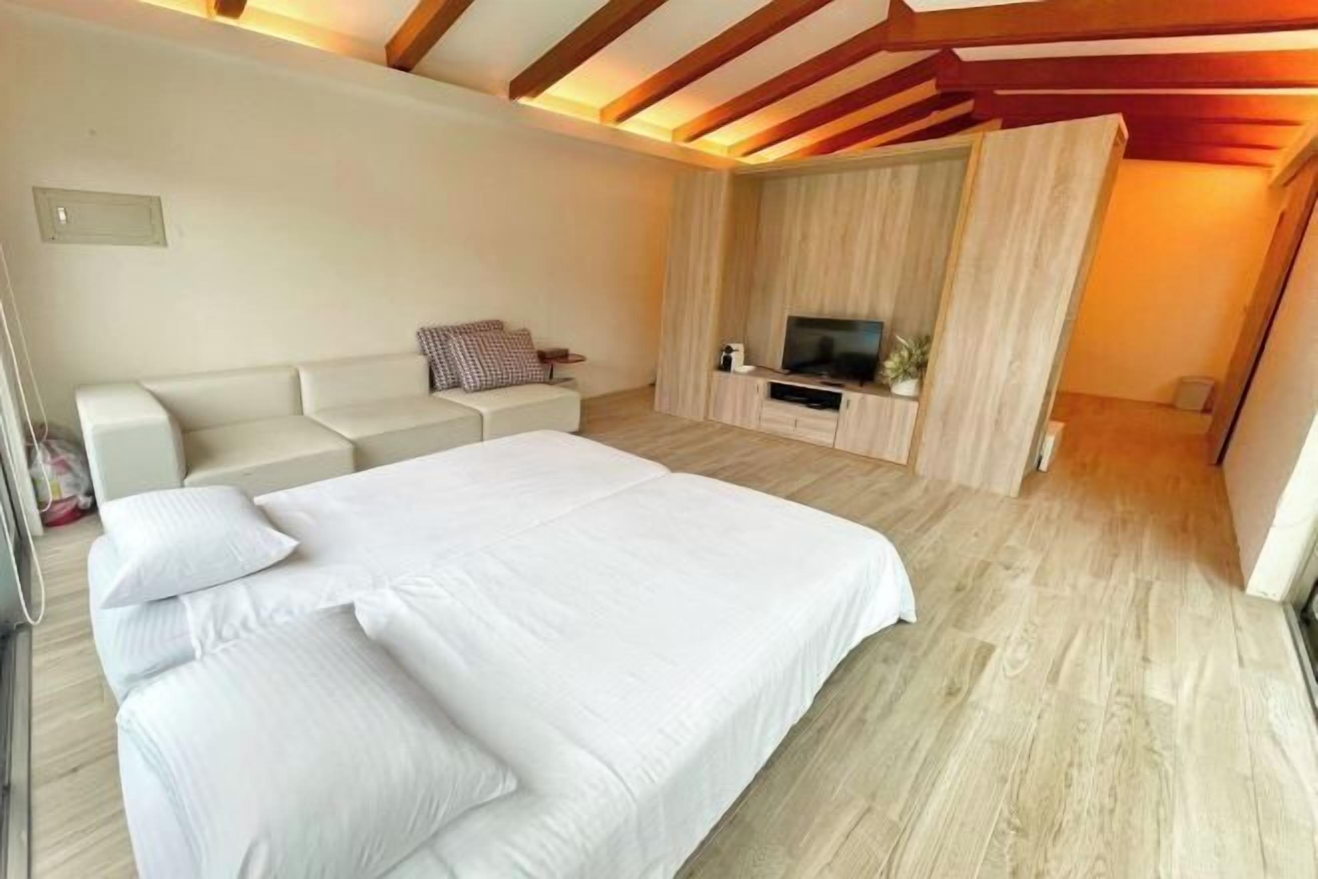 A bedroom with a large bed, a sofa, a TV, and wooden flooring.