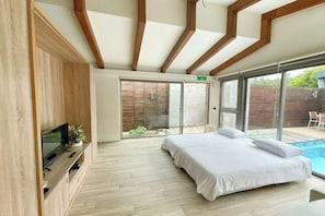 Un dormitorio moderno con cama, televisor y puerta corrediza de vidrio que da a una zona de piscina.