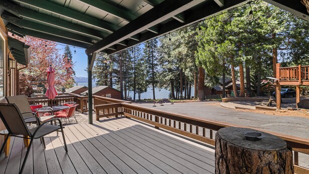 Une terrasse en bois offrant une vue sur un lac et des arbres, avec des meubles d’extérieur et un espace abrité doté d’une rambarde.