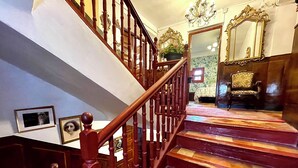 A grand staircase with wooden railings and a chandelier, leading to a room with a large mirror and a patterned carpet. - RIOJANIA HEREDAD (Santa Eulalia Bajera)