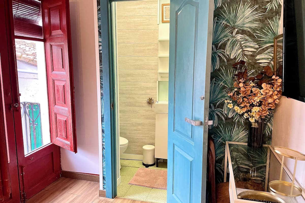 Een gang met een rode deur, een blauwe deur en een glazen deur naar een badkamer.