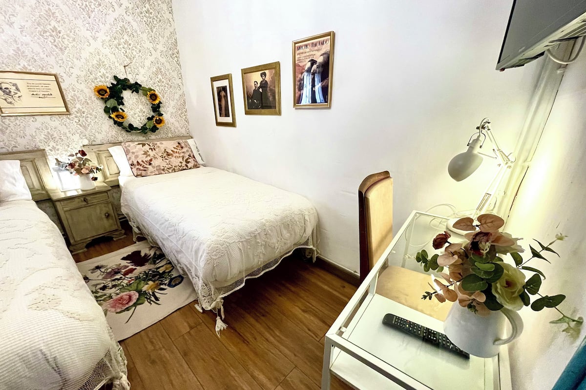 Een slaapkamer met een bed, nachtkastjes, een bureau met lamp en lijstjes aan de muur.