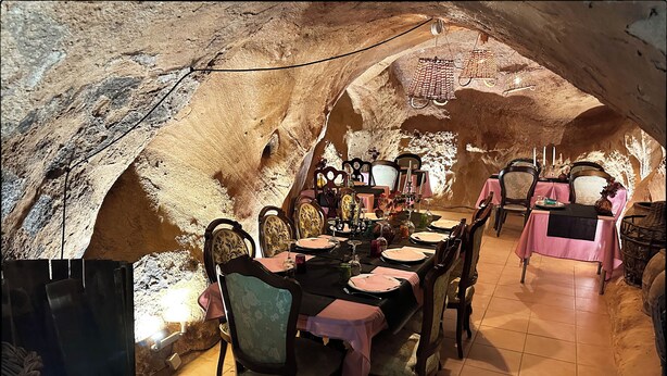 An underground dining area with rustic stone walls, wooden tables, and chairs. - RIOJANIA HEREDAD (Santa Eulalia Bajera)