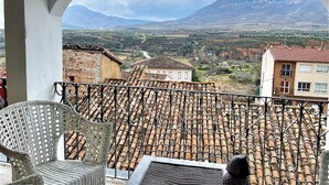 A balcony with a view of a mountainous landscape, a rustic building with a tiled roof, and a white chair. - RIOJANIA HEREDAD (Santa Eulalia Bajera)
