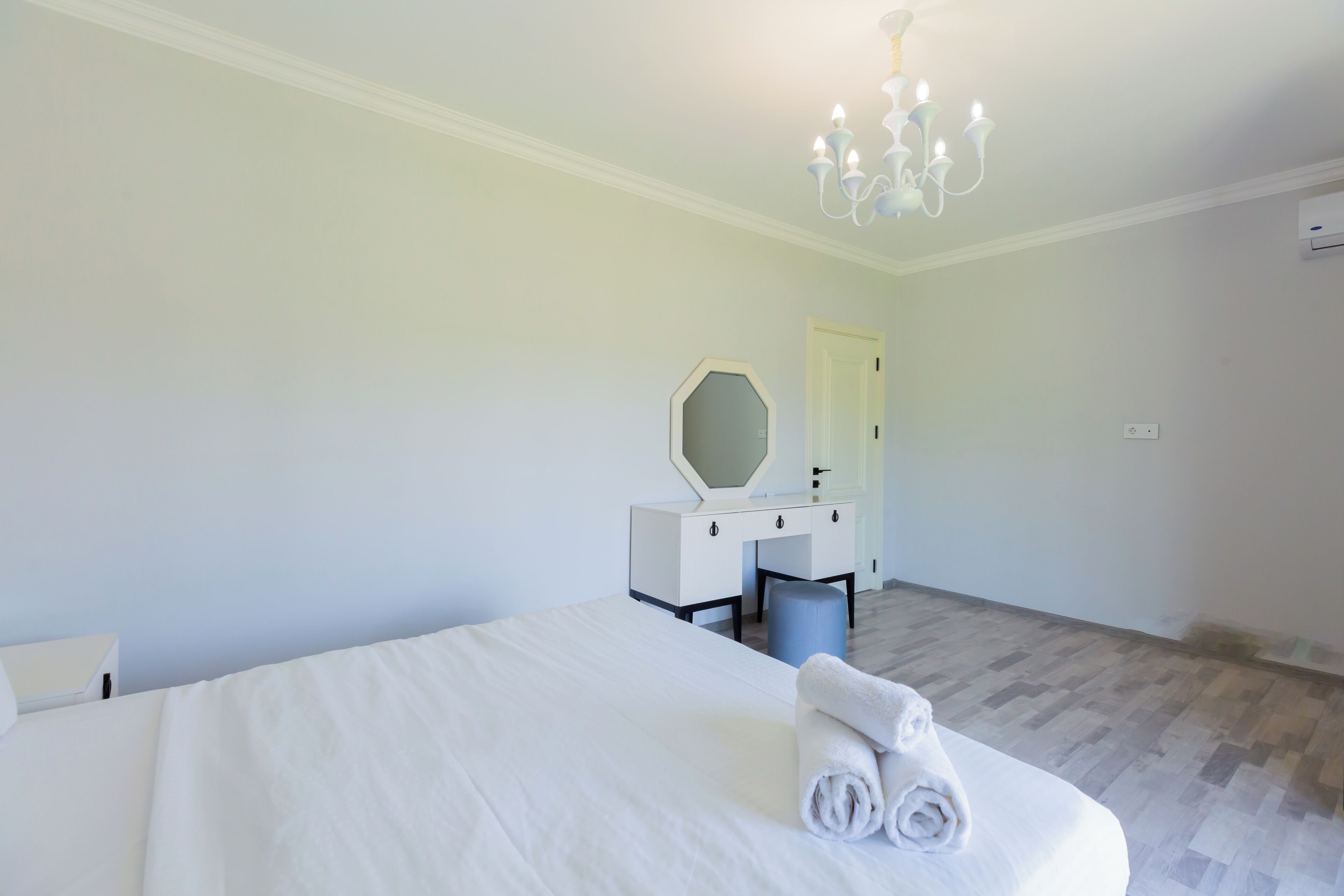 A hotel room with a large bed, a bedside table, a mirror, and a chandelier.