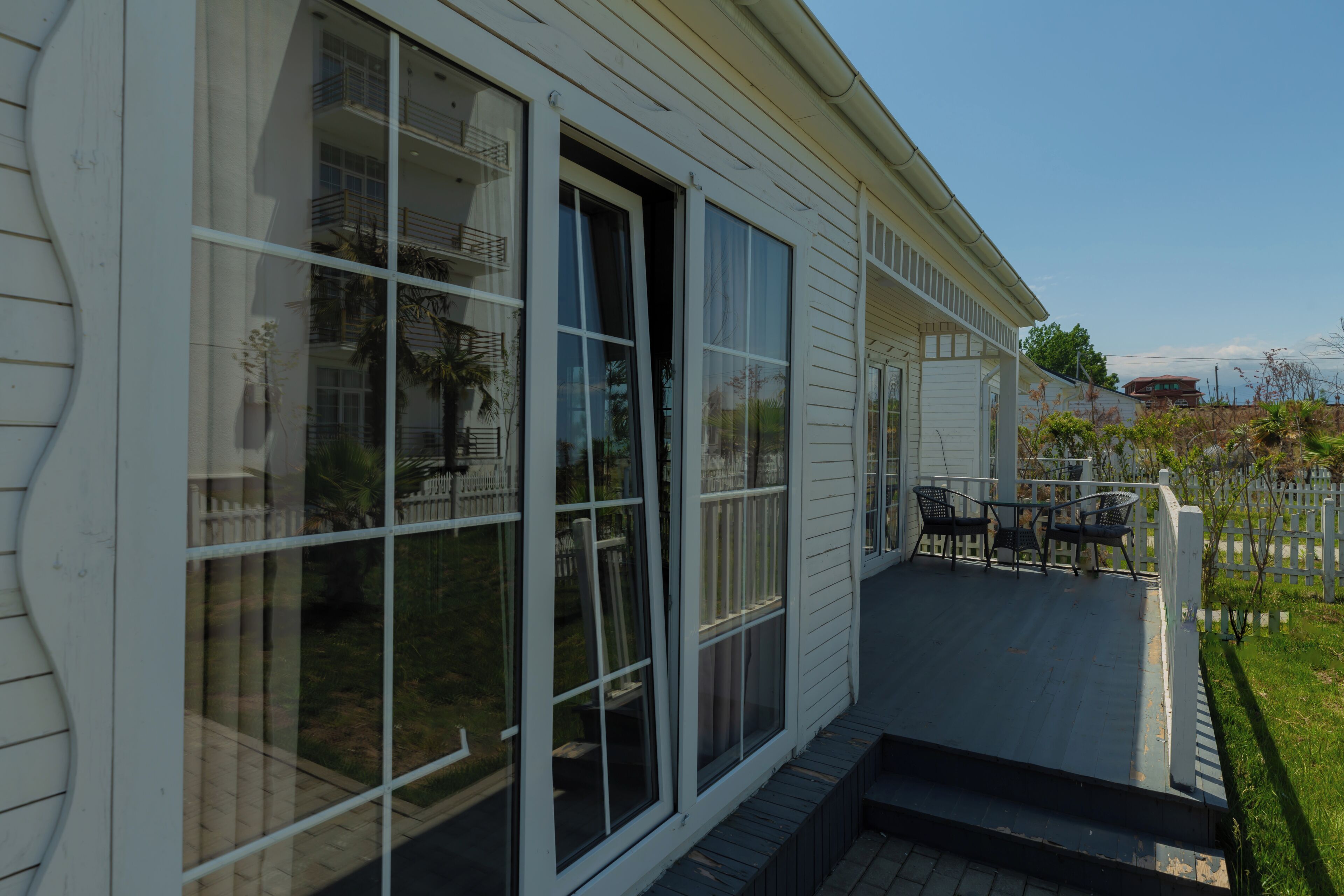 A white house with large windows, a covered porch with outdoor furniture, and a white picket fence.