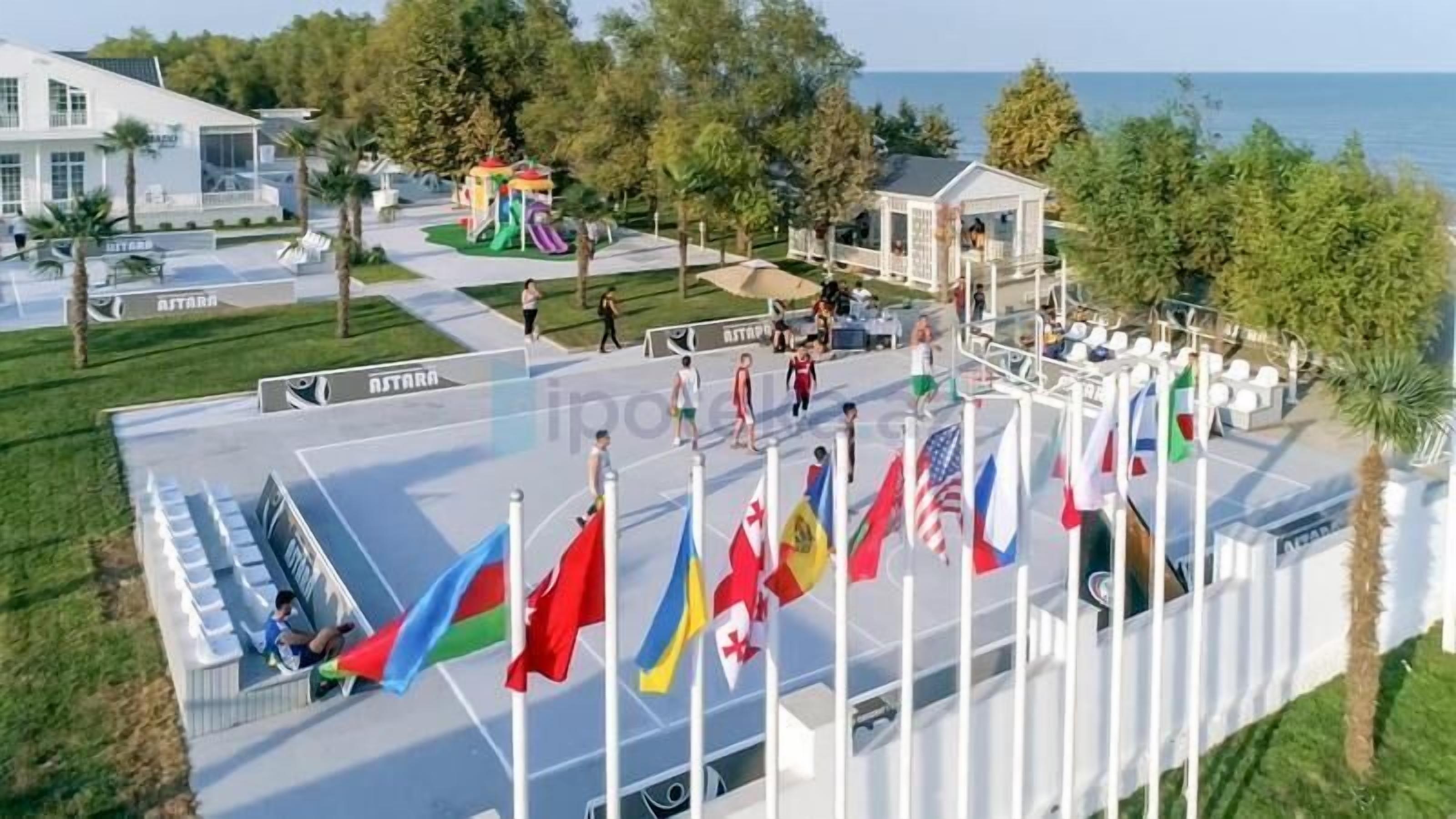 Instalación deportiva con pista de atletismo, zona de juegos infantiles y varias banderas.