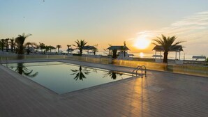Ein Swimmingpool mit Sonnenuntergangsblick, umgeben von Palmen und schattigen Sitzbereichen.