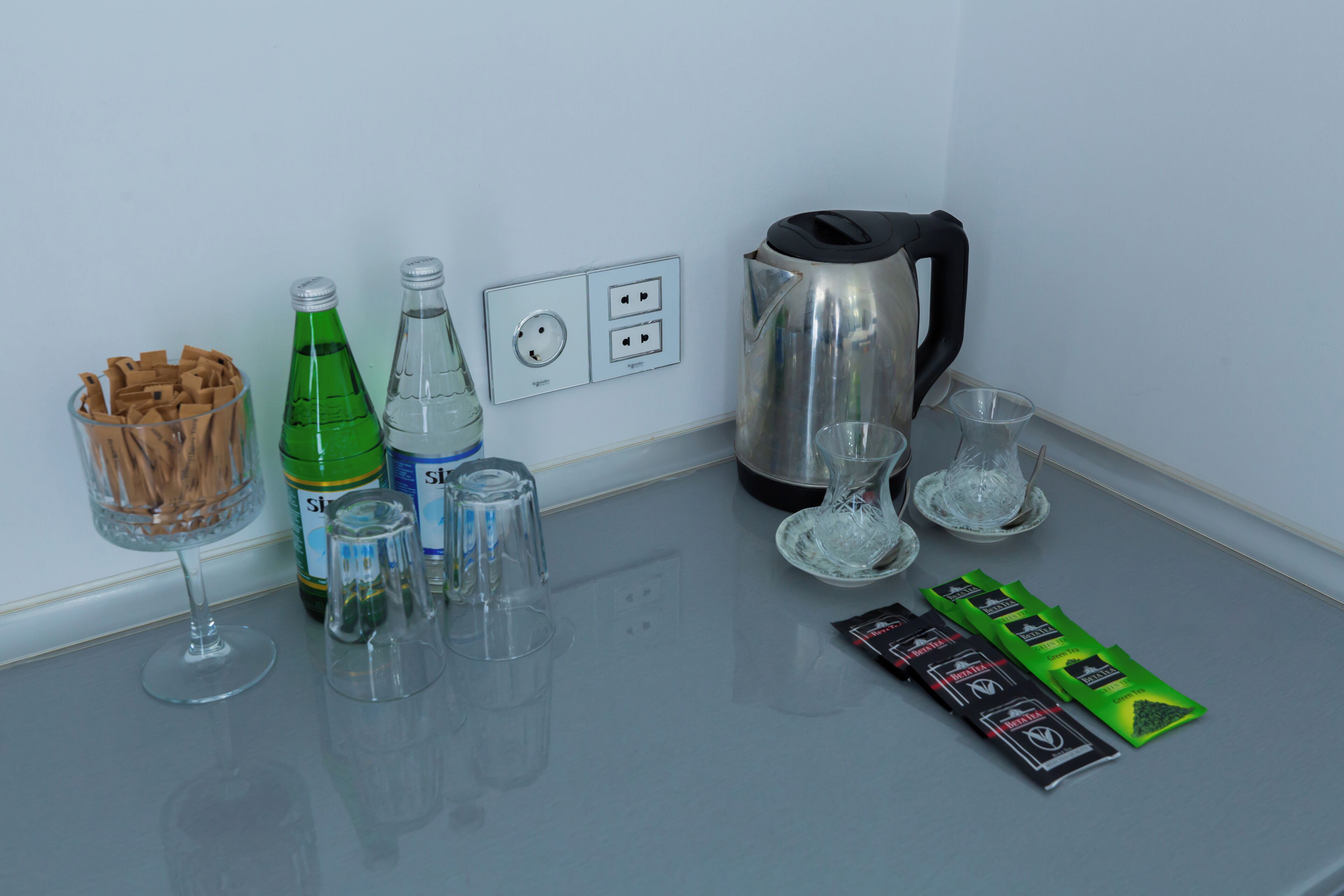 Una encimera de cocina con una copa de vino, una botella de agua, una tetera, un vaso, un paquete de aperitivos y un vaso de chocolate.