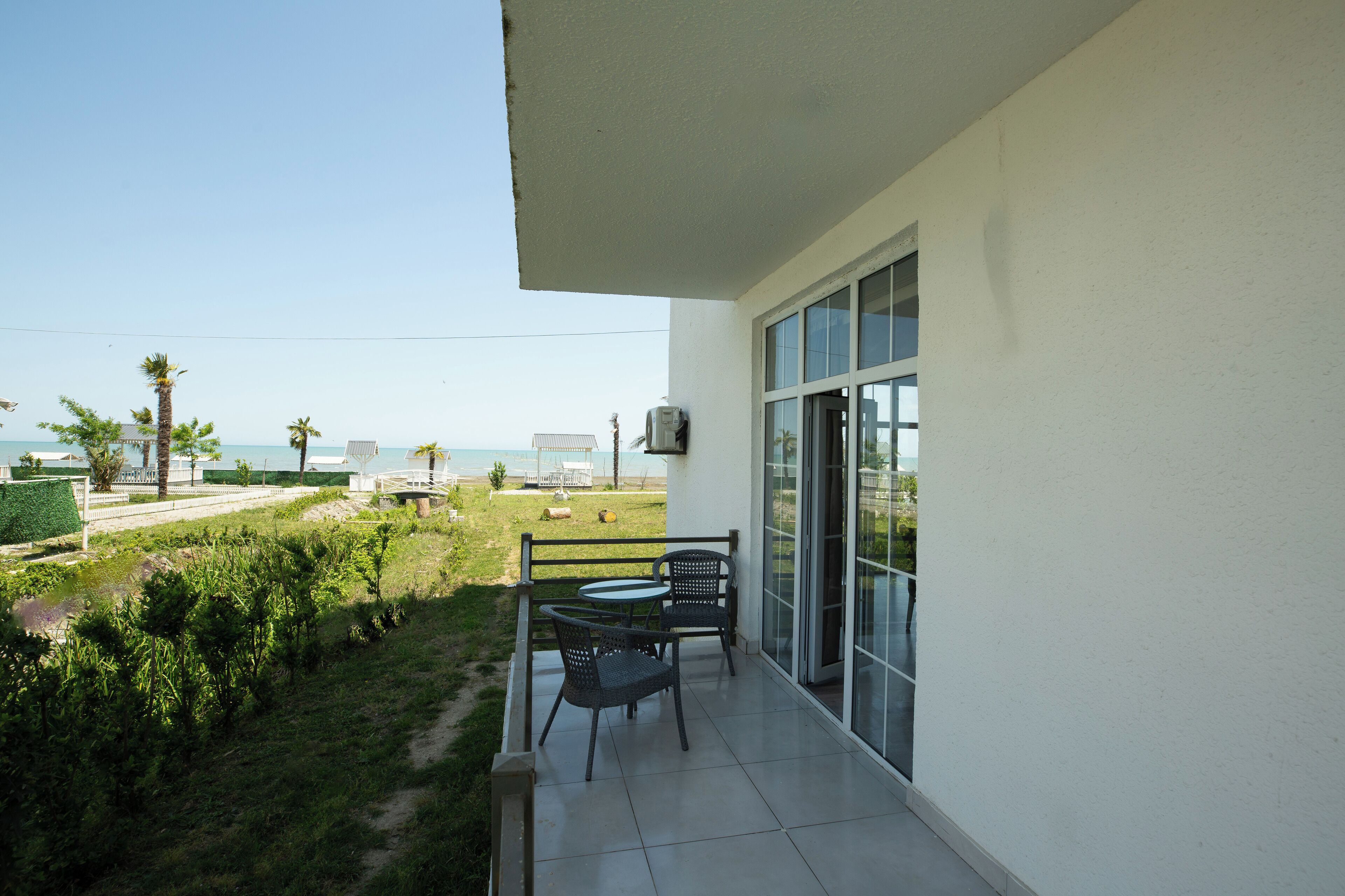 A balcony with two chairs and a table, overlooking a grassy area with a view of the sea.