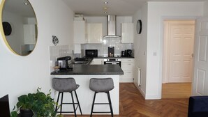 A modern kitchen with white cabinets, a black countertop, and two bar stools. - Charming 2 bedroom apartment, recently refurbished, great location pet friendly! (Anlaby)