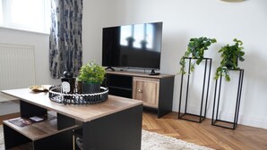 A modern living room with a wooden coffee table, a television, a cabinet, and two potted plants. - Charming 2 bedroom apartment, recently refurbished, great location pet friendly! (Anlaby)