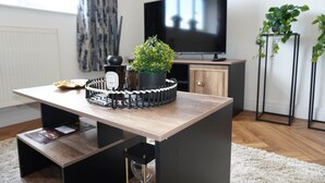A modern living room with a wooden table, a potted plant, a decorative item, and a television. - Charming 2 bedroom apartment, recently refurbished, great location pet friendly! (Anlaby)