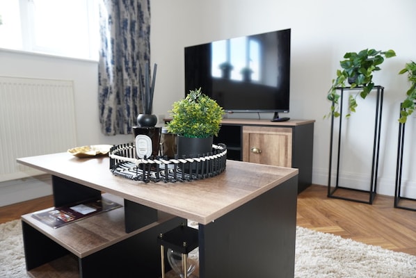 A modern living room with a wooden table, a potted plant, a decorative item, and a television.