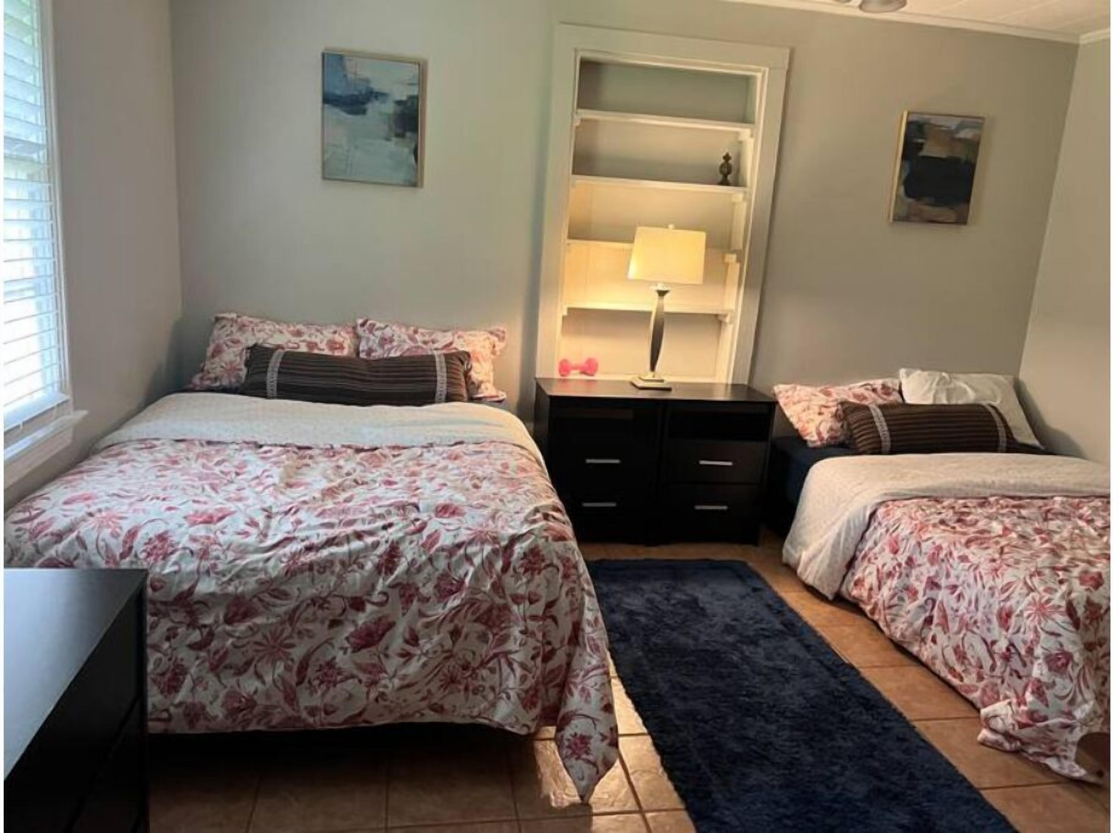A bedroom with two beds, a desk, a dresser, and a nightstand.