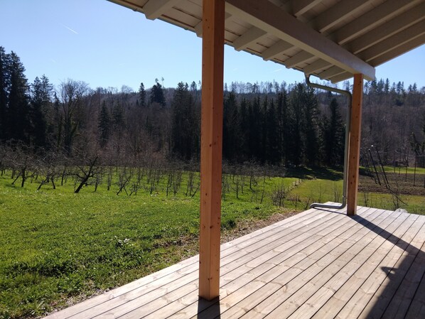 A wooden deck with a view of a vineyard and forest.
