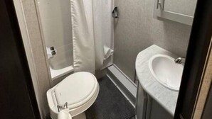 A compact bathroom with a skylight, a toilet, a shower, and a sink.