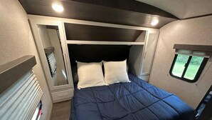 A compact bed with a headboard, a small window, and a storage unit with a mirror.