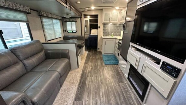 A compact RV interior with a sofa, kitchenette, and a TV.