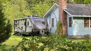 A camper parked in front of a house with a chimney.