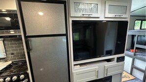 A compact kitchen with a built-in refrigerator, a microwave, a stove, and a large flat-screen TV.