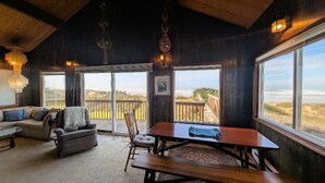 Un interno accogliente con soffitto in legno, un divano, un tavolo e sedie. Ampie finestre offrono vista sulla spiaggia e sull'oceano.