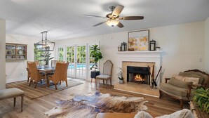Un salon spacieux doté d’une cheminée, d’un ventilateur de plafond et d’un coin repas avec des chaises en osier.