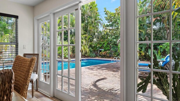 A pool area with a clear view through large glass doors, a pool, and surrounding greenery. - Sawfish Bay Bungalow Old Florida Charm (Jupiter)