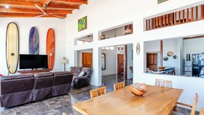 A spacious living area with a wooden dining table, leather sofas, and surfboards on the wall. - Beachfront AC Villa, 3BR, 3.5BA,  great surfing! Free Parking (Guanacaste Province)