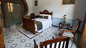 A bedroom with a bed, a chair, a small table, a chandelier, and patterned floor tiles.
